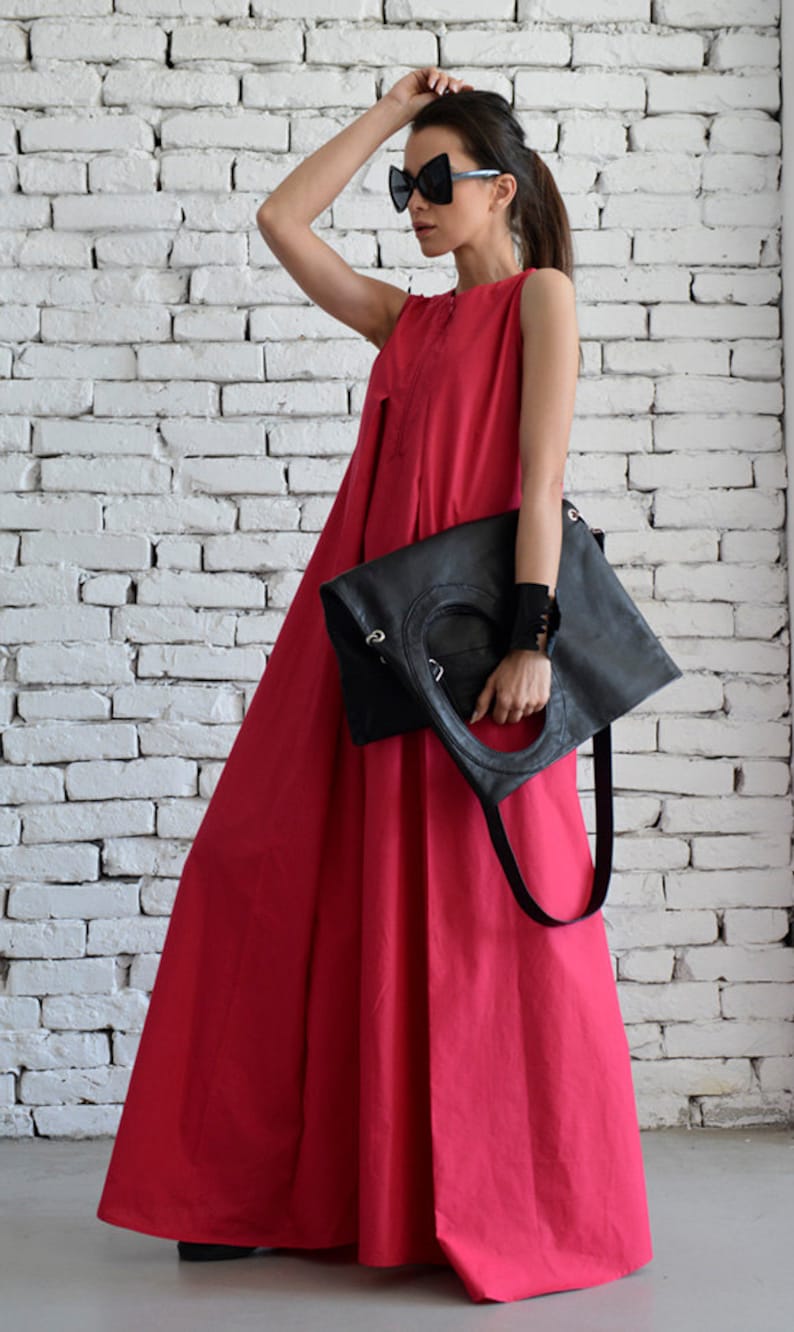 May include: A woman wearing a bright pink sleeveless maxi dress and black sunglasses holds a black leather tote bag with a long strap.