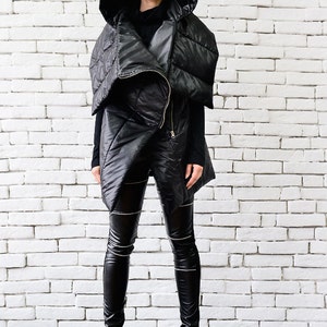 May include: A black hooded puffer vest with a zipper closure. The vest is worn over a black turtleneck and black leggings. The person is wearing black sunglasses and black heeled boots.