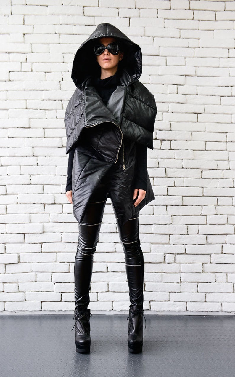 May include: A black hooded puffer vest with a zipper closure. The vest is worn over a black turtleneck and black leggings. The person is wearing black sunglasses and black heeled boots.