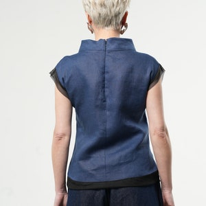 May include: A navy blue linen top with a black trim and short sleeves. The top has a high neckline and a zip at the back.