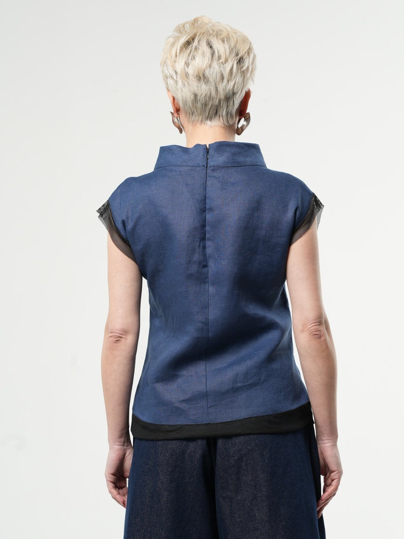 May include: A navy blue linen top with a black trim and short sleeves. The top has a high neckline and a zip at the back.