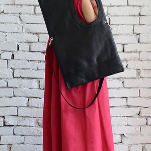 May include: A woman wearing a red dress and sunglasses holds a black leather tote bag with a circular cutout. The bag has a long strap.