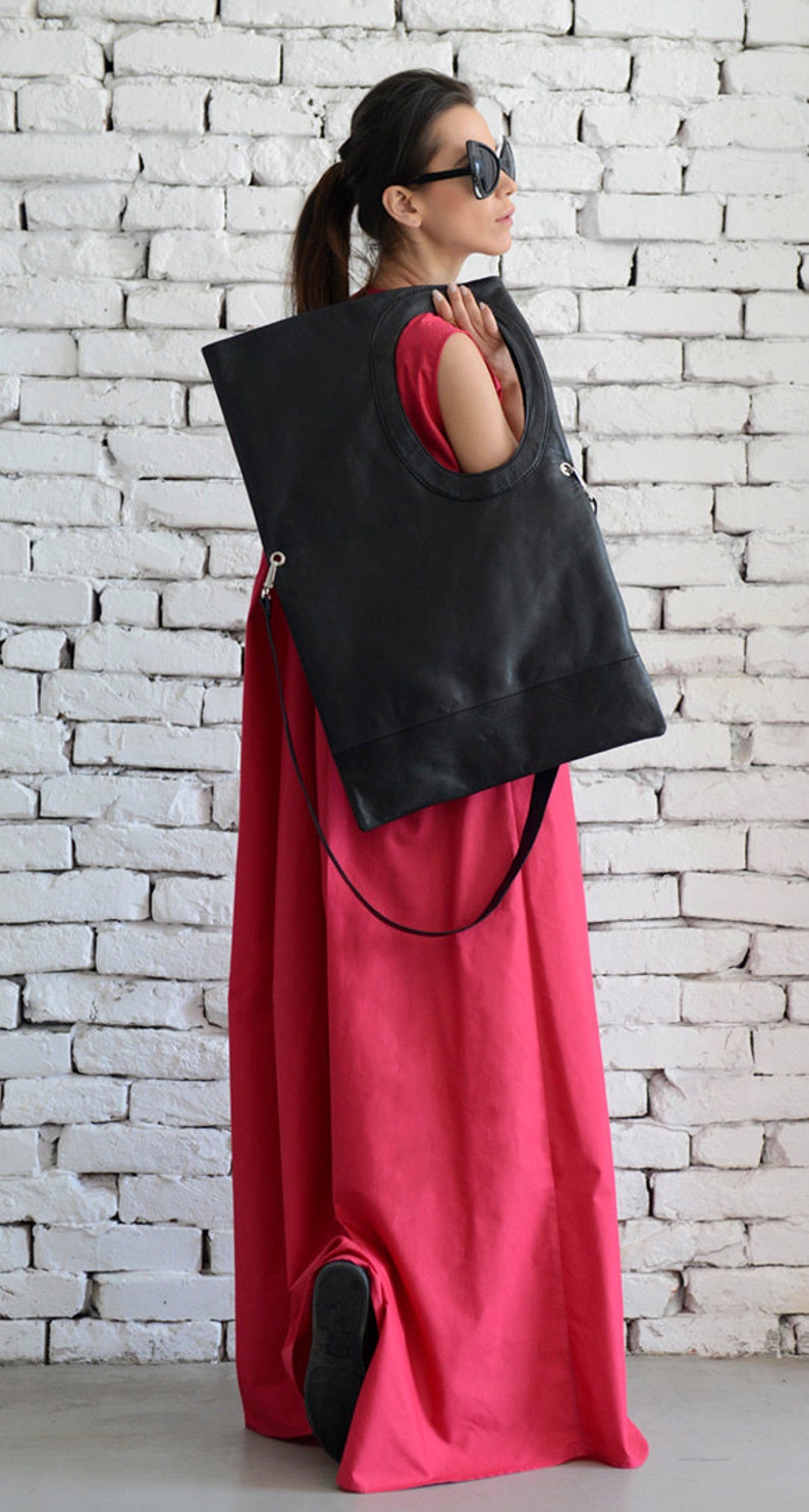 May include: A woman wearing a red dress and sunglasses holds a black leather tote bag with a circular cutout. The bag has a long strap.