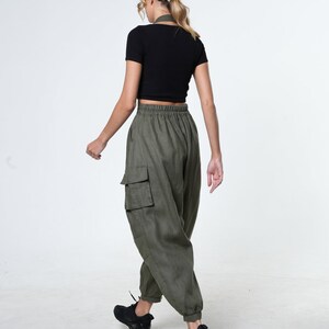 May include: A woman wearing a black crop top and olive green cargo pants with a drawstring waist. She is wearing black sneakers.