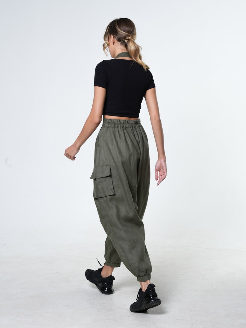 May include: A woman wearing a black crop top and olive green cargo pants with a drawstring waist. She is wearing black sneakers.
