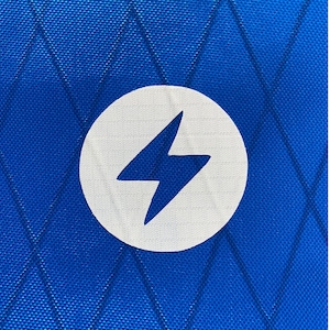 May include: A close-up of a blue fabric with a white circle containing a lightning bolt symbol.