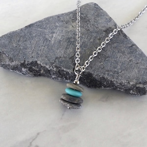 May include: A silver chain necklace with a pendant made of stacked stones. The stones are gray and a light blue color.