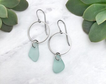 May include: A pair of silver hoop earrings with a light blue sea glass charm hanging from each hoop.