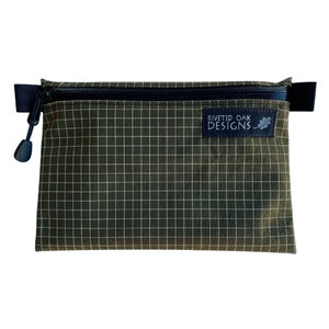 May include: A green zippered pouch with a grid pattern and the text "Riveted Oak Designs" on a black label.