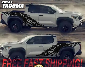 Puede incluir: Una camioneta Tacoma blanca 2024+ con una calcomanía gráfica en blanco y negro en el lateral. La calcomanía presenta la palabra "Tacoma" y un diseño estilizado de pista de tierra. La camioneta se muestra sobre un fondo de tierra marrón. El texto "FREE FAST SHIPPING!" se muestra en letras rojas con un emoji sonriente. Los textos "WATERPROOF", "UV PROTECTION", "OUTDOOR DURABILITY - LIFETIME", "AMERICAN MADE" y "PREMIUM MATTE VINYL" se enumeran con marcas de verificación.
