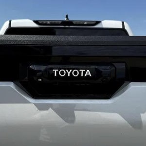 May include: A silver pickup truck with the word "TUNDRA" embossed on the tailgate and the word "TOYOTA" on the back of the truck bed.