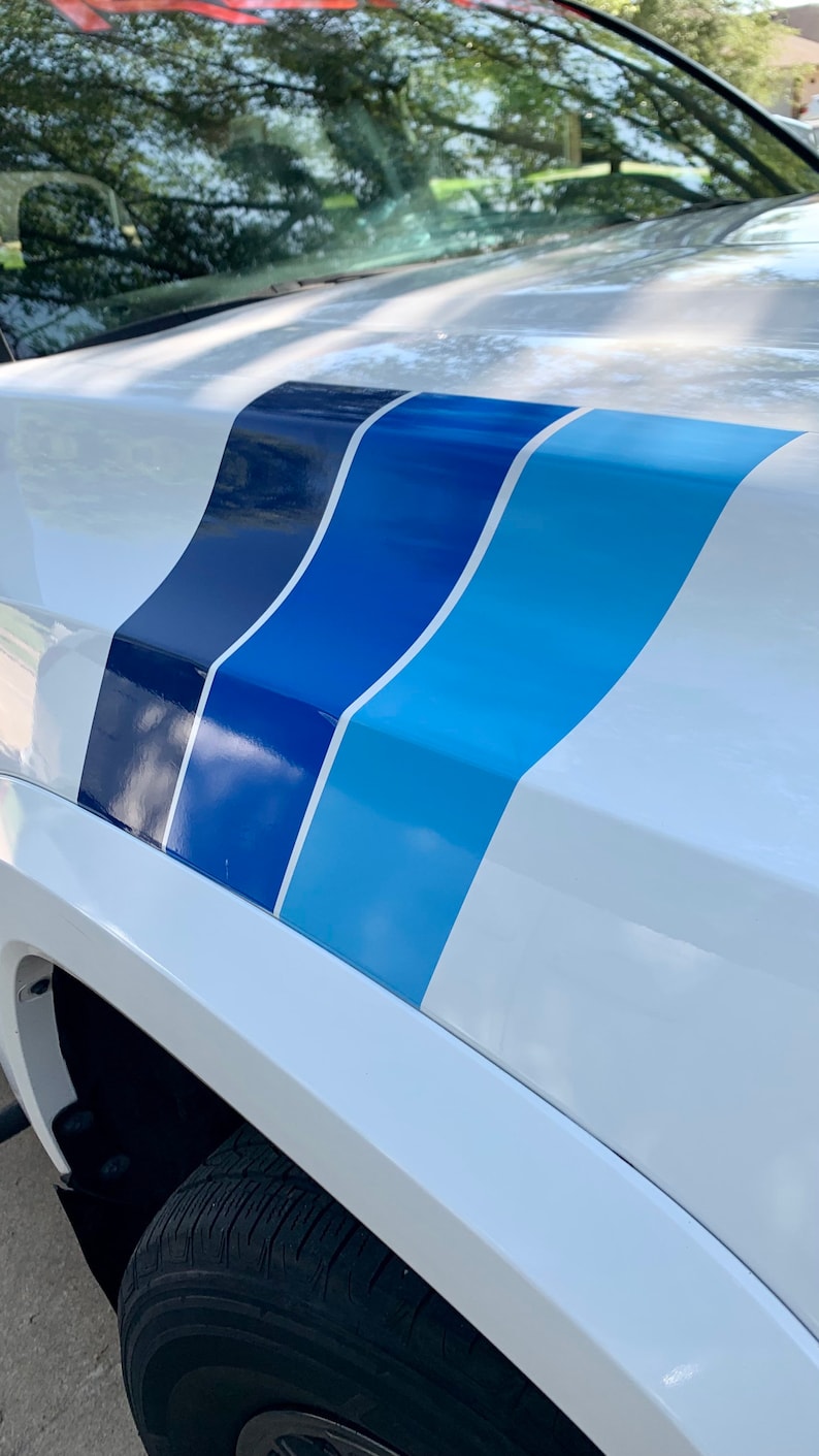 May include: White car with a blue, light blue, and dark blue racing stripe decal on the hood.