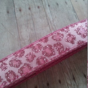May include: Pink ribbon with a glitter leopard print design. The ribbon has a woven edge and a light pink background. The leopard spots are a darker pink and covered in glitter. This ribbon is suitable for crafts and gift wrapping.