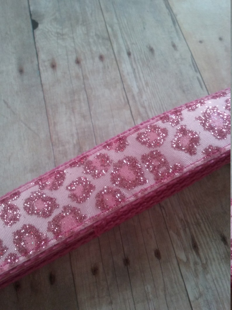 May include: Pink ribbon with a glitter leopard print design. The ribbon has a woven edge and a light pink background. The leopard spots are a darker pink and covered in glitter. This ribbon is suitable for crafts and gift wrapping.
