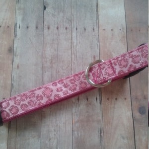 May include: Pink dog collar with a glittery leopard print design. The collar features a silver metal D-ring and a black buckle. The collar is made of a durable material and is designed for pets.