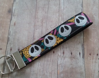 May include: A black key chain with a colorful patterned ribbon featuring multiple white Jack Skellington faces. The ribbon is attached to a silver key ring.