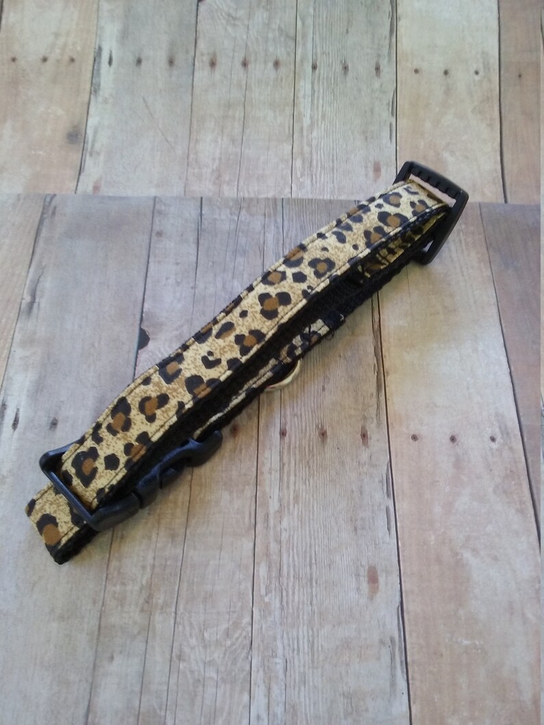 May include: A black and brown leopard print dog collar with a black plastic buckle.