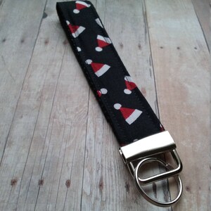 May include: A black and white key chain with a red and white Santa hat pattern. The key chain has a silver metal ring and a silver metal clasp.