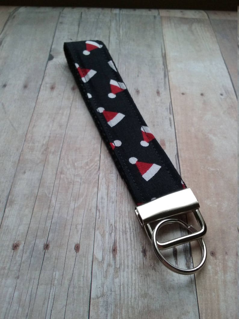 May include: A black and white key chain with a red and white Santa hat pattern. The key chain has a silver metal ring and a silver metal clasp.
