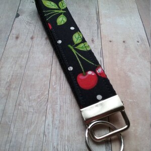 May include: Black and white fabric key chain with a red cherry print and white polka dots. The key chain has a silver metal ring.
