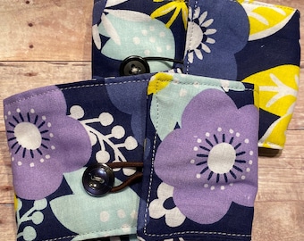 May include: Three fabric pouches with a floral pattern in shades of blue, purple, yellow, and white. Each pouch has a brown elastic band and a black button closure.