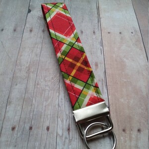 May include: A red, green, and yellow plaid fabric keychain with a silver key ring.