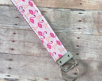 May include: Pink flamingo key chain with a silver key ring. The key chain is made of fabric with a pink flamingo pattern.