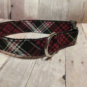 May include: A black, red, and white plaid dog collar with a silver metal D-ring.