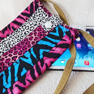 May include: A colorful tablet sleeve with a variety of animal print patterns, including zebra, leopard, and cheetah prints in pink, black, and blue. The sleeve has a tan strap and a white snap closure. An iPad is partially visible.