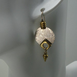 May include: Silver and gold tone earrings with a geometric design. The earrings feature a round disc with a textured pattern and a dangling spike.
