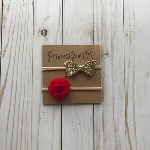 May include: Two baby headbands on a brown card. One headband has a gold glitter bow, and the other has a red felt flower. The card has the text "Princess Bows US" in gold script.