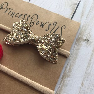 May include: A gold glitter bow headband with the text "Princess Bows US" on a brown card. The headband is made of a thin, beige elastic band.