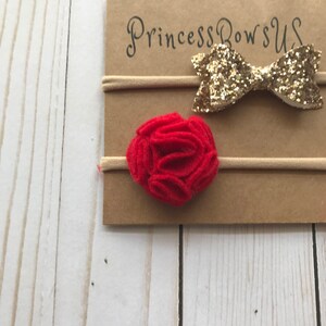 May include: Two baby headbands on a cardboard backing. One headband features a gold glitter bow, and the other has a red felt flower. The cardboard is printed with the text "Princess Bows US". The background is a light wood.