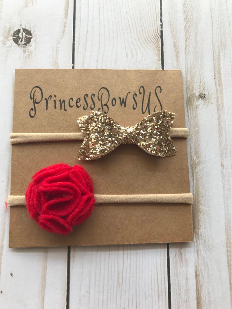 May include: Two baby headbands on a brown card. One headband has a gold glitter bow, and the other has a red felt flower. The card has the text "Princess Bows US" in black script.