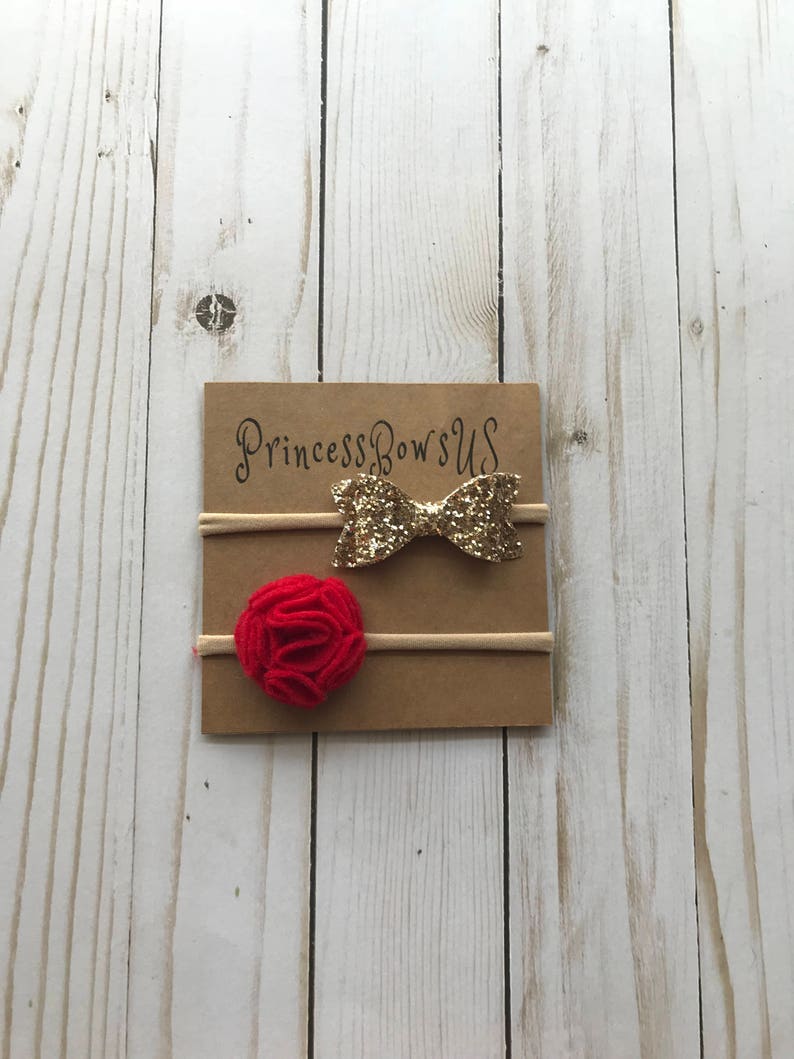 May include: A set of two baby headbands on a brown card. One headband features a gold glitter bow, and the other has a red felt flower. The card has the text "PrincessBowsUS" in a script font.