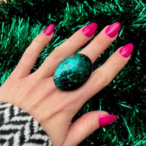 May include: A large oval ring with a dark green base and a sparkly teal glitter finish.