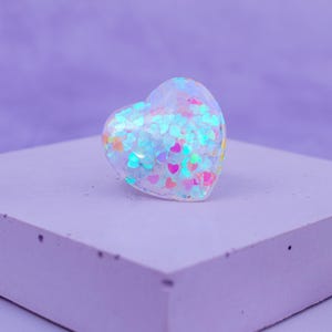 May include: A clear heart-shaped resin ornament filled with iridescent glitter and small pink hearts.
