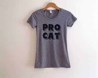 Op de afbeelding: Grijs T-shirt met korte mouwen met een zwarte afbeelding met de tekst "PRO CAT" in vetgedrukte blokletters.