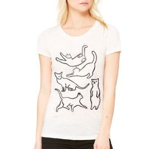 May include: White t-shirt with a black outline of five cats stacked on top of each other.