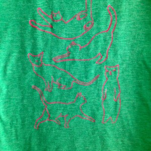 May include: Green t-shirt with a pink outline of five cats stacked on top of each other.
