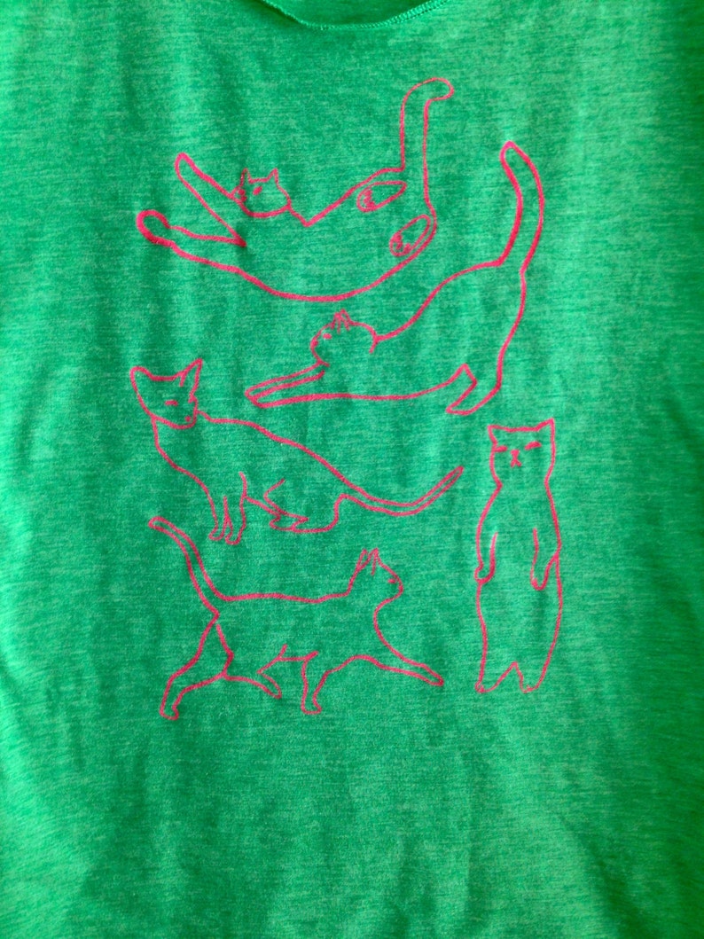 May include: Green t-shirt with a pink outline of five cats stacked on top of each other.
