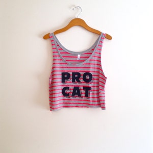 Op de afbeelding: Een grijs en roze gestreept tanktop met de tekst "PRO CAT" in zwarte letters.