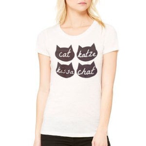 May include: White t-shirt with four black cat silhouettes and the words "cat", "katze", "kissa", and "chat" written in white.