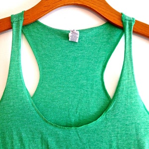 May include: A green tank top with a red graphic on the front. The tank top is hanging on a wooden hanger.