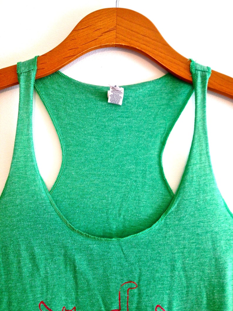 May include: A green tank top with a red graphic on the front. The tank top is hanging on a wooden hanger.