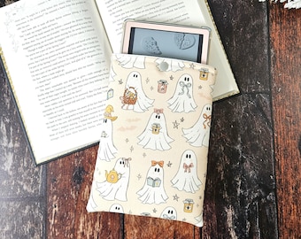 Pode incluir: Uma capa para leitor de e-books bege e branca com um padrão de fantasmas fofinhos segurando xícaras de chá, livros e potes de mel. A capa tem um fecho de correr e é projetada para se ajustar a um leitor de e-books padrão.