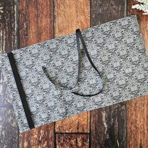 May include: A gray fabric book roll with a black ribbon tie and a repeating pattern of open books. The fabric has a subtle texture.