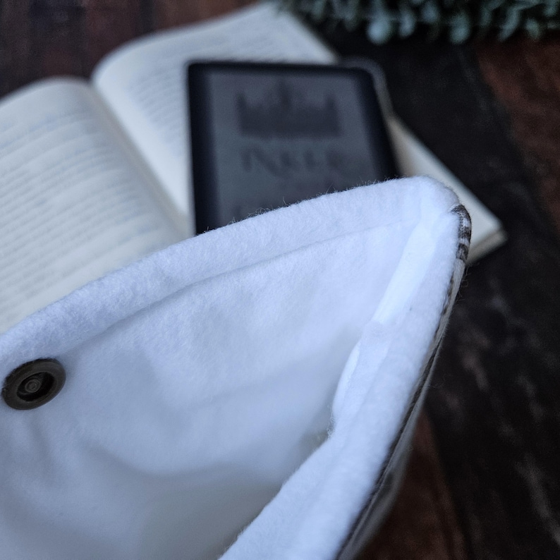 K&ouml;nnte beinhalten: Nahaufnahme des Innenraums einer wei&szlig;en und grauen Buchh&uuml;lle. Die H&uuml;lle ist mit weichem, wei&szlig;em Fleece gef&uuml;ttert und hat einen Knopfverschluss.