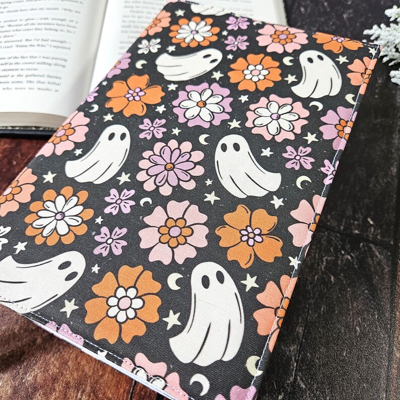 May include: A black fabric book cover with a repeating pattern of white ghosts, orange and pink flowers, and white stars.