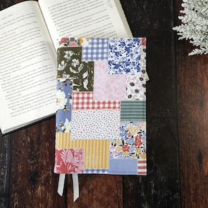 May include: A book cover with a patchwork design featuring various floral patterns, gingham, and stripes in shades of blue, pink, red, yellow, and green.